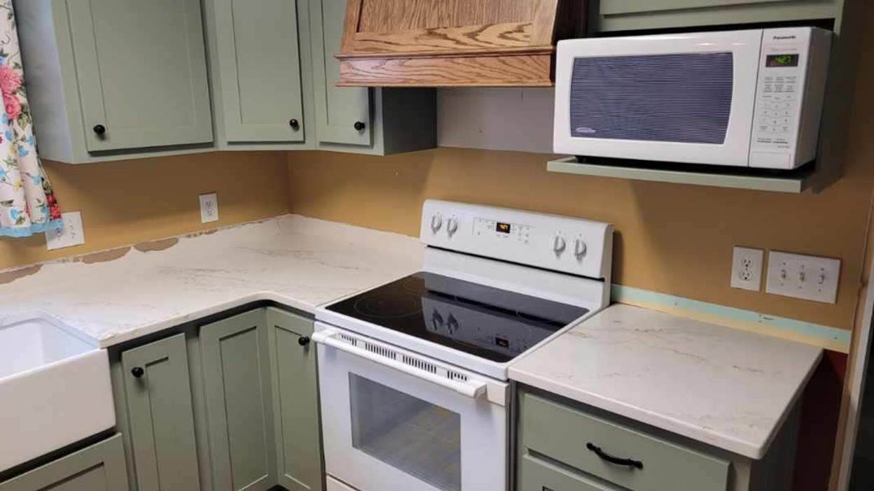 A kitchen with white stove and green cabinets

Description automatically generated