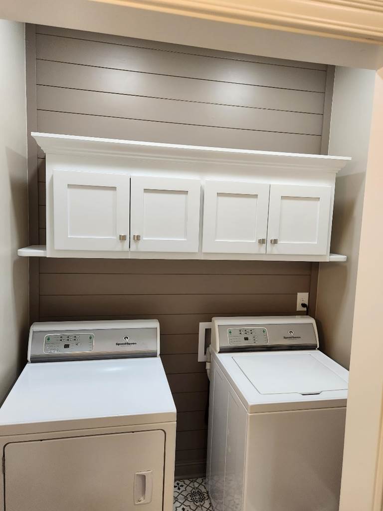 A laundry room with white cabinets and dryers

Description automatically generated